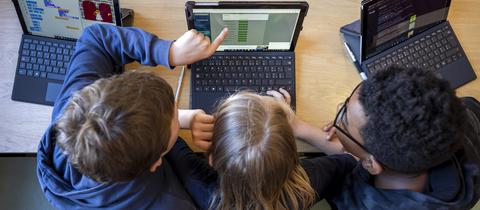 Drei Schüler zeigen auf Laptop
