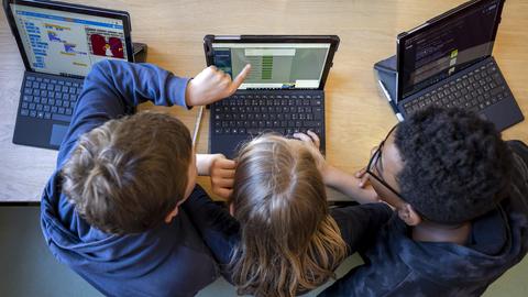 Drei Schüler zeigen auf Laptop