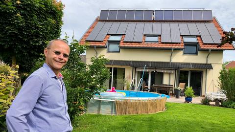 Mann steht vor einem Einfamilienhaus mit Solarkollektoren und Photovoltaikanlage