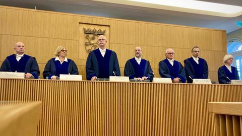 Die Mitglieder des Staatsgerichtshofs stehen im Gerichtssaal an ihren Plätzen.