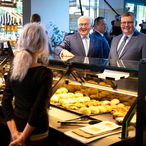 Bundessprräsident Steinmeier, Einweißhaarigermann, Mit Einem Beleibten Mann ein Einembäckerstandauf Einem Wegenmarkt. Die Beidenverkäerinnensind von Hinten Zu Sehen. DIEBEDEN MANNER LACHEN.