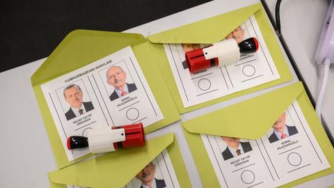 Vier Wahlzettel liegen auf einem Tisch, darauf je Name und Foto der beiden Kandidaten und Stempel zum Abstimmen