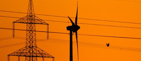 Ein Windrad neben einem Strommast vor rotem Himmel.