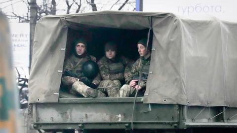 Drei ukrainische Soldaten in Uniform sitzen auf der Pritsche eines Militärfahrzeugs.