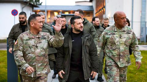 Der ukrainische Präsident Selenskyj läuft zwischen Militäroffizieren bei einem Besuch der US-Streitkräfte in Wiesbaden im Dezember 2023.
