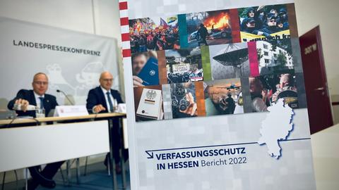 Broschüre Verfassungsschutzin Hessen - Bericht 2022 - im Hintergrund sitzt Innenminister Beuth - an der Wand steht Landespresskonferenz