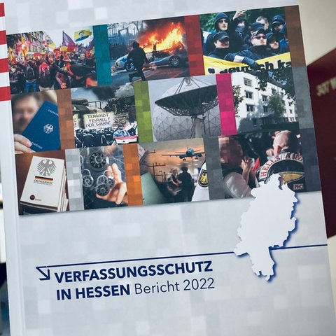 Broschüre Verfassungsschutzin Hessen - Bericht 2022 - im Hintergrund sitzt Innenminister Beuth - an der Wand steht Landespresskonferenz