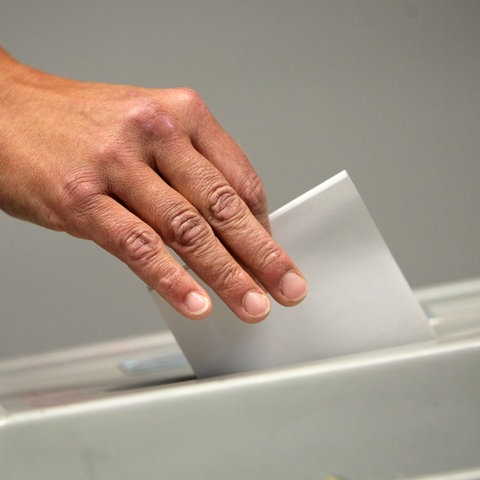 Eine Wählerin steckt bei der Wahl seinen Wahlzettel in eine Urne.
