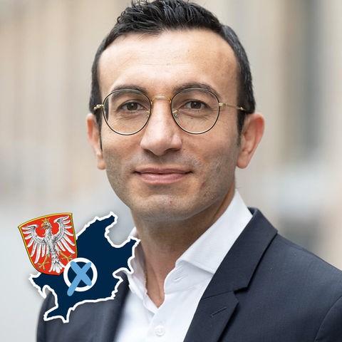 Portraitfoto von Mike Josef. Auf dem Foto eine kleine Grafik mit einer blau eingefärbten Fläche (Umriss Stadt Frankfurt), dem Wappen der Stadt Frankfurt und einem Wahlkreuz.