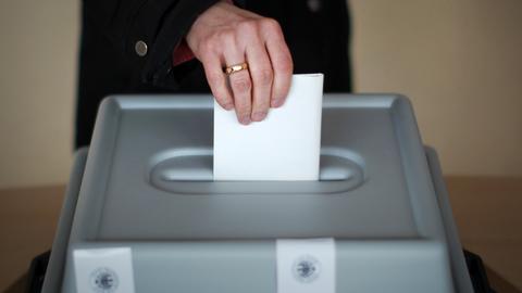 Eine Hand steckt einen Umschlag in eine versiegelte Wahlurne