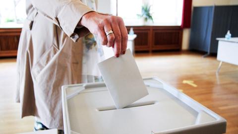 Eine Hand steckt einen Umschlag in eine versiegelte Wahlurne