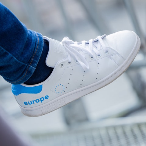 Ein weißer Turnschuh hat auf der Außenseite das Wort "europe" in hellblauer Schrift eingeprägt