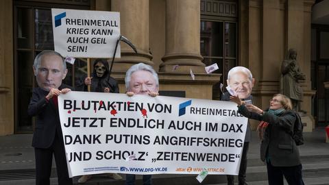 Gegen die Aufnahme des Rüstungskonzerns Rheinmetall in den Dax protestieren Aktivisten vor der Börse in Frankfurt mit einem Plakat auf dem steht "Blutaktien von Rheinmetall jetzt endlich auch im DAX Dank Putins Angriffskrieg und Scholz' Zeitenwende".