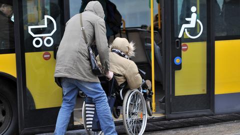 Eine Person im Rollstuhl wird von einer anderen Person in einen Bus geschoben.