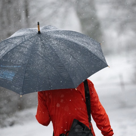 Eine Frau geht mit Regenschirm durch den Schnee. 