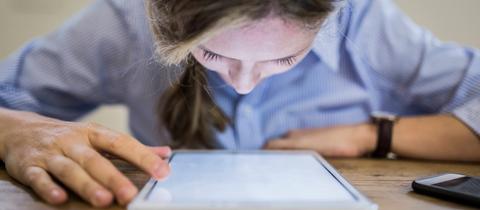 Frau sitzend, Gesicht hängt über leuchtendem Display eines Tablets.