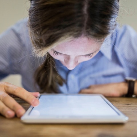 Frau sitzend, Gesicht hängt über leuchtendem Display eines Tablets.