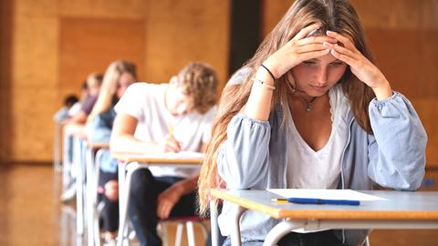 Prüfungssituation im Klassenzimmer mit grübelndem Mädchen und Klassenkameraden