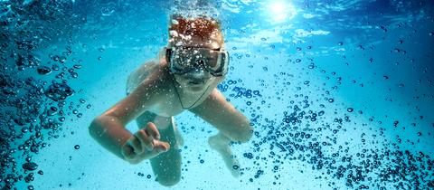 Ein Junge mit großer Tauchermaske im aufgewirbelten Wasser