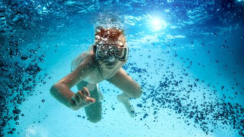 Ein Junge mit großer Tauchermaske im aufgewirbelten Wasser