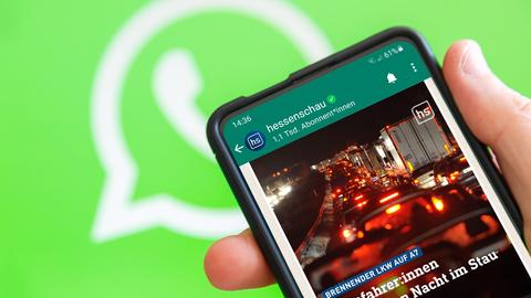 Vor einem grünen Hintergund mit einem WhatsApp-Logo ein Smartphone mit hessenschau-WhatsApp-Chat auf dem Bildschirm.