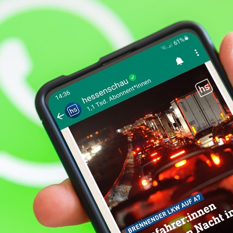 Vor einem grünen Hintergund mit einem WhatsApp-Logo ein Smartphone mit hessenschau-WhatsApp-Chat auf dem Bildschirm.