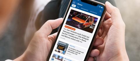 Sitzende Person mit Handy in der Hand, auf dem Handy ist die hessenschau App zu sehen