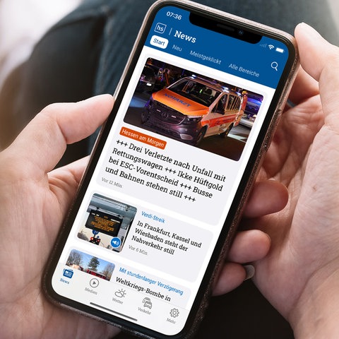 Sitzende Person mit Handy in der Hand, auf dem Handy ist die hessenschau App zu sehen