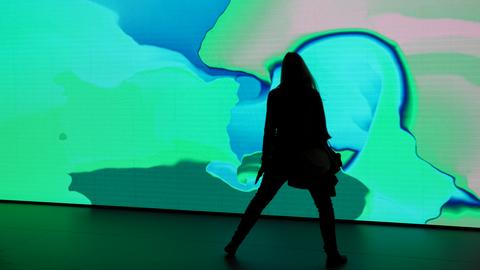 Frau steht vor interaktiver Leinwand mit grün-blauen Farben