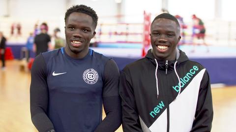 Die Brüder Hansen stehen in Sportkleidung in einer Halle und lachen in die Kamera