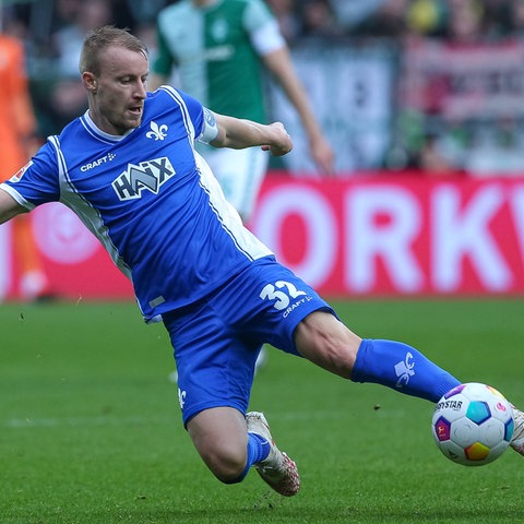 Fabian Holland (in blauem Darmstadt-Trikot) wirft sich in einen Ball. 
