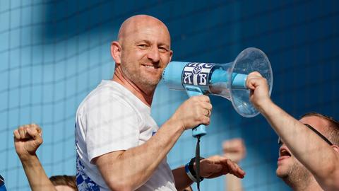 Darmstadts Trainer Lieberknecht mit Megaphone und breitem Grinsen auf dem Zaun.