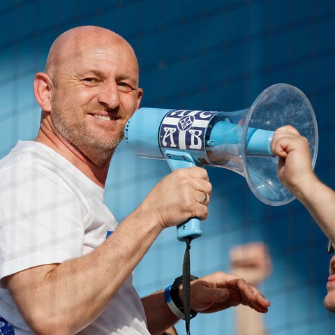 Darmstadts Trainer Lieberknecht mit Megaphone und breitem Grinsen auf dem Zaun.