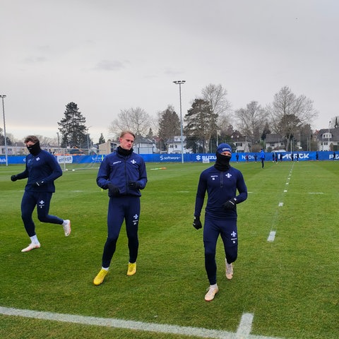 Mehrere Darmstadt-Spieler laufen sich warm. Wegen der kalten Temperaturen tragen sie langärmlige dunkelblaue Trainingsanzüge, Handschuhe, Schals und Mützen. 