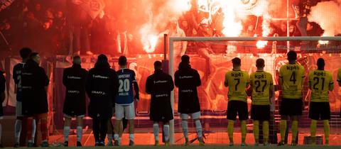 Die Spieler von Darmstadt 98 und BSC Young Boys stehen vor der Tribüne, wo Pyros gezündet werden.