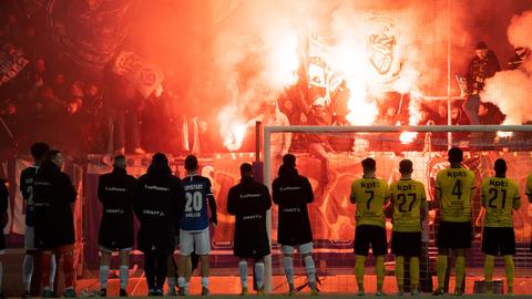 Die Spieler von Darmstadt 98 und BSC Young Boys stehen vor der Tribüne, wo Pyros gezündet werden.