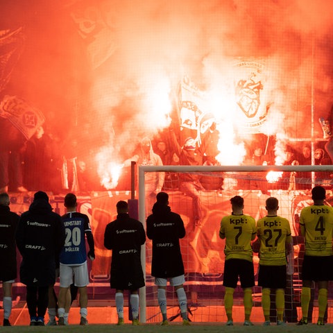 Die Spieler von Darmstadt 98 und BSC Young Boys stehen vor der Tribüne, wo Pyros gezündet werden.