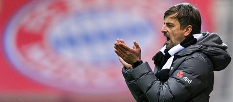 Eintracht-Trainer Niko Arnautis steht vor dem Emblem des FC Bayern und applaudiert