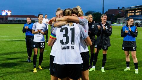 Drei Fußballerinnen jubeln und umarmen sich. Andere stehen drumherum und klatschen.