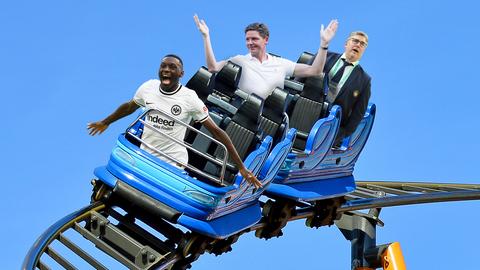 Collage: Randal Kolo Muani, Oliver Glasner und Axel Hellmann sitzen in einer Achterbahn.