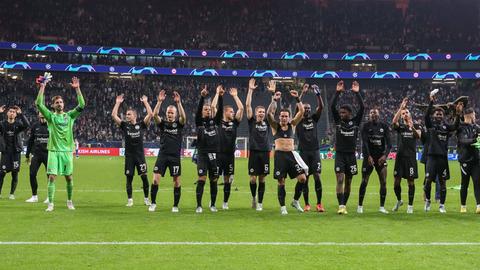 Eintracht Frankfurt-Fußballer stehen in einer Reihe auf dem Fußballrasen und werfen ihre Arme hoch.
