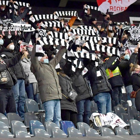 Viele Fans auf den Rängen eines Stadions, die gestreifte Schals in die Höhe halten.