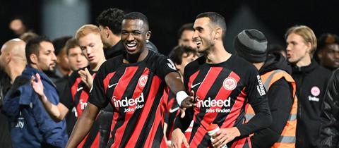 Zwei Fußballspieler in schwarz-rot gestreiften Trikots lachen.