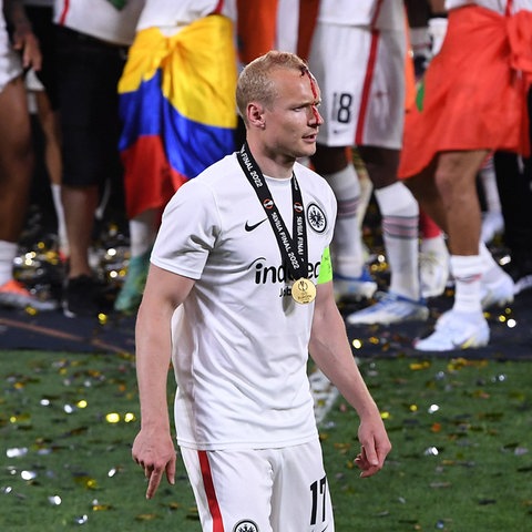 Sebastian Rode läuft im Bildvordergrund (scharf) Unscharf im Bildhintergrund feiernde Fußball-Fans. 