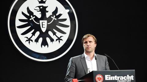 Markus Krösche im Rampenlicht vor einem großen Eintracht-Logo. 