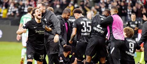 Jubelnde Fußballspieler in schwarzen Trikots bilden einen Haufen auf einem Spielfeld.