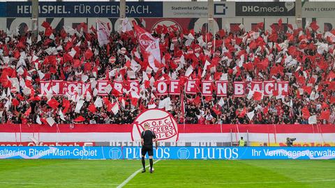 Das Bild zeigt eine Fankurve im Stadion der Kickers Offenbach. Die Zuschauer wehen rote und weiße Fahnen. 