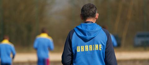 Spieler der ukrainischen Handball-Nationalmannschaft trainieren auf einem Platz. Auf den blauen Sweatshirts ist der Schriftzug "Ukraine" zu sehen.