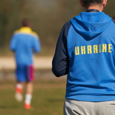 Spieler der ukrainischen Handball-Nationalmannschaft trainieren auf einem Platz. Auf den blauen Sweatshirts ist der Schriftzug "Ukraine" zu sehen.