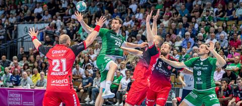 Drei Handballspieler der MT Melsungen (rote Trikots) kämpfen mit zwei Spielern der HSG Wetzlar um den Ball (grüne Trikots). 